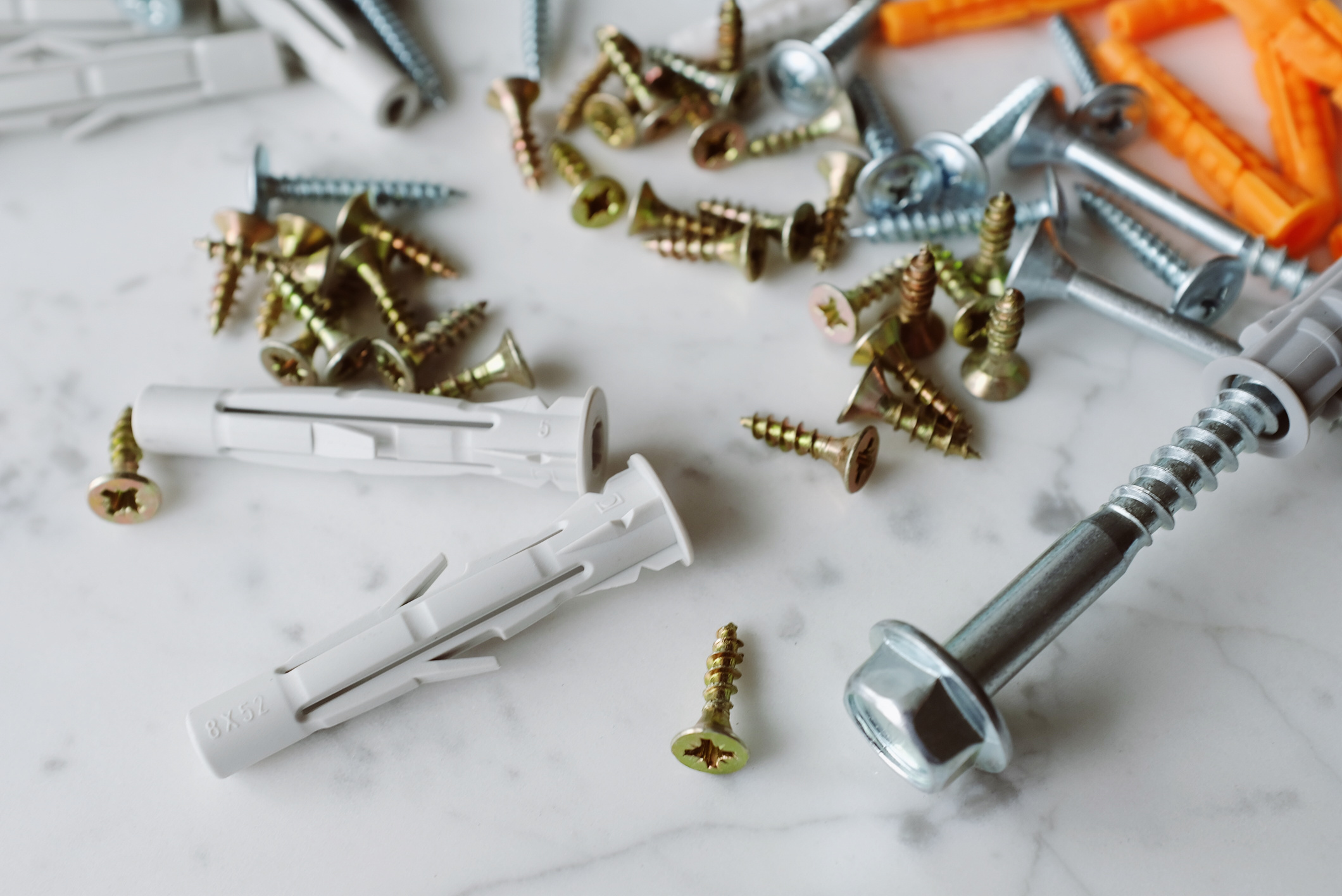 Bunch of various screws and dowels placed on marble table in workshop
